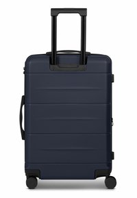 Maleta rígida azul marino con superficie texturizada, asa negra retráctil, cuatro ruedas y costuras decorativas en los lados.