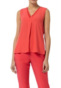 Koronkowa bluzka bez rękawów w kolorze koralowym z dekoltem w szpic i plisowanym przodem, wykonana z gładkiego materiału; zestawiona z dopasowanymi koralowymi spodniami.