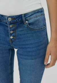 High-waisted blue denim jeans with a five-button fly, two front pockets, and a slim fit. Smooth texture with subtle fading details.