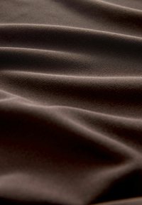 Brauner Stoff mit einer weichen, glatten Textur, der sanfte Falten und ein mattes Finish aufweist, was subtile Variationen von Licht und Schatten erzeugt.