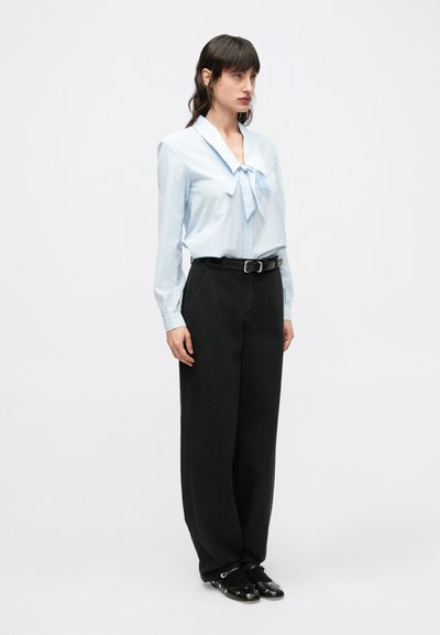 Blusa de rayas azul claro con cuello grande y detalle de lazo, combinada con pantalones negros de pierna ancha de talle alto y zapatos negros sin cordones.