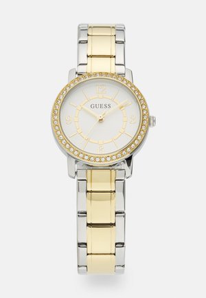 Orologio rotondo in acciaio inossidabile con bracciale in maglia metallica argento e oro. Il quadrante bianco presenta dettagli dorati e una lunetta ornata di cristalli.