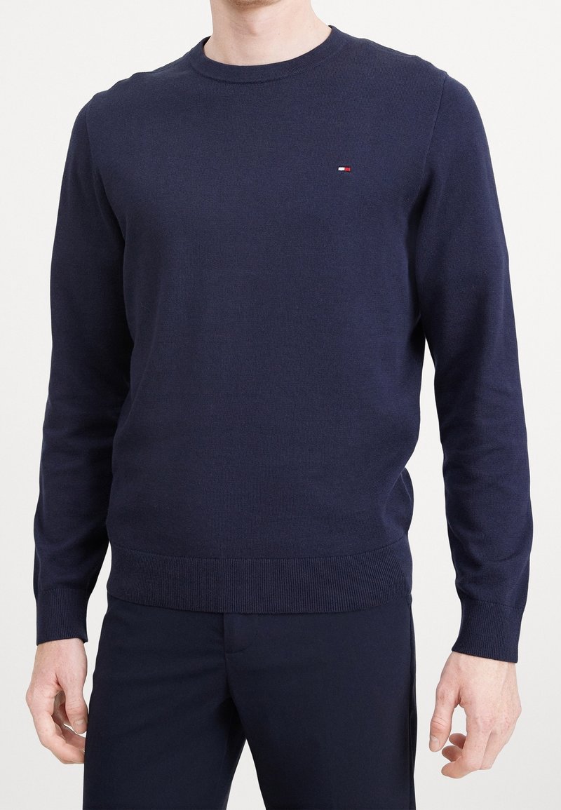 Granatowy sweter z dzianiny o okrągłym dekolcie, z prążkowanymi mankietami i dołem. Posiada małe, haftowane logo na piersi. Miękka tekstura i dopasowany krój.