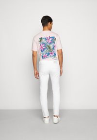 Lys rosa t-shirt med et farverigt blomsterprint på ryggen, parret med hvide jeans og hvide sneakers. Enkel design og tætsiddende pasform.