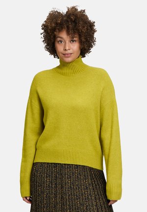 Pull en col montant vert citron en tricot doux et texturé avec des poignets et un ourlet côtelés, associé à une jupe plissée sombre ornée d'un imprimé léopard.