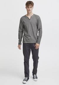 Graues Langarm-Henley-Shirt mit drei Knöpfen am Halsausschnitt, kombiniert mit dunklen Hosen und schwarzen Sneakers. Einfaches Design und lässige Passform.