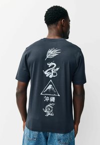 Fekete pamut póló, amelyen fehér grafikák láthatók a hátoldalon: egy levél, sárkány, hegy és koi hal. Rövid ujjú, kerek nyakú.