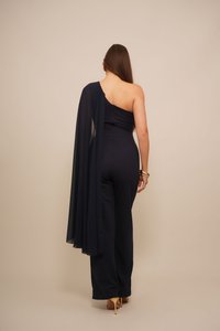 Navy blue one-shoulder haalari, johon kuuluu virtaava, läpinäkyvä päällinen. Tiukka muotoilu leveillä lahkeilla. Varustettu piilotetulla takataskulla. Kulta-pronssiset asusteet.