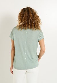 Top corto de manga corta verde claro con un acabado texturizado, que presenta un cierre de botones en la parte de atrás y un dobladillo acanalado. Diseño sencillo con un ajuste relajado.