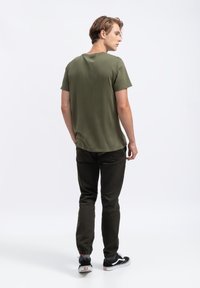 Olijfgroen katoenen T-shirt met een ronde hals, gecombineerd met donkergroene taps toelopende broeken en zwarte sneakers met witte zolen.
