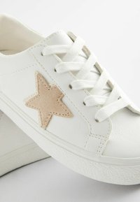 Le sneaker bianche in pelle presentano un accento in suede beige a forma di stella, un design con lacci e una suola bianca testurizzata. Si concentrano su linee pulite e uno stile minimalista.