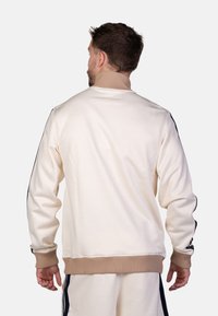 Beige sweatshirt met een ribbelkraag en -manchetten, met marineblauwe zijstrepen en een gladde textuur; ontworpen voor een ontspannen pasvorm.