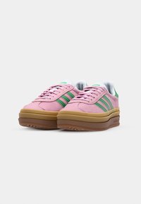 Pink suede sneakers with green stripes, white accents, and a brown rubber sole. Laces and padded tongue complete the design.