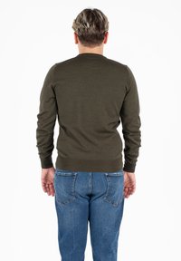 Maglione lavorato a maglia verde oliva con maniche lunghe, polsini a coste e scollatura rotonda. Indossato con jeans blu, dotati di tasche posteriori.