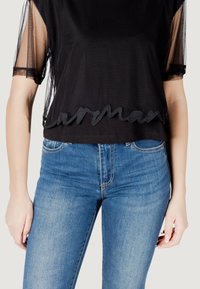 Top nero a maniche corte con maniche in rete trasparente, caratterizzato da un orlo ondulato ricamato. Abbinato a jeans in denim blu.