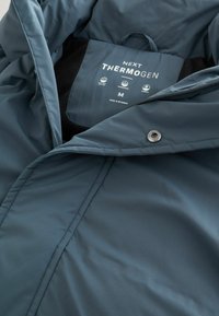 Blaue wasserdichte Jacke mit einem weichen schwarzen Innenfutter, Reißverschluss und einem Markenetikett mit Pflegeanweisungen und Größe.