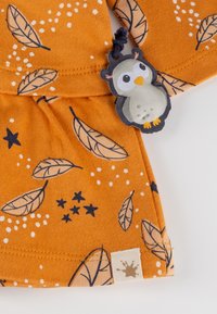 Oranger Stoff mit Blatt- und Sternmuster. Enthält ein Etikett mit einem niedlichen Eulendesign. Weiche Textur und einfacher, verspielter Stil.