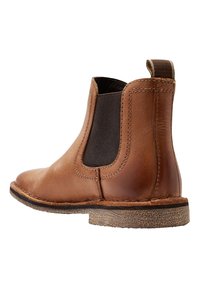 Stivale Chelsea in pelle marrone con pannelli laterali elasticizzati, suola texture e punta rotonda. Presenta un linguetta sul retro per una facile calzata.