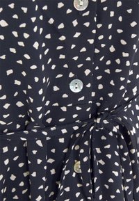 Robe en tissu marine avec un motif éclaboussé blanc, présentant un devant à boutons, des boutons ronds et un détail de taille nouée.