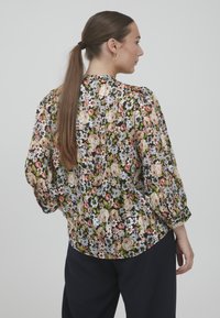 Blusa floreale con sfondo nero e fiori multicolori. Maniche lunghe con dettagli arricciati. Tessuto leggero e semitrasparente.