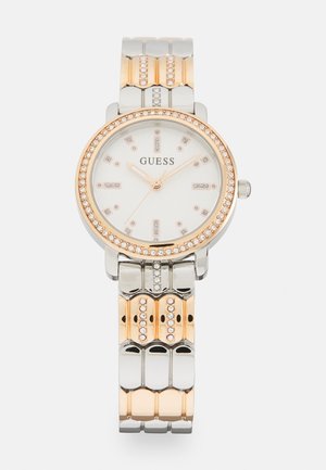 Montre ronde en argent et or rose avec une lunette ornée de cristaux, un cadran blanc et un bracelet métallique présentant des textures et motifs alternés.