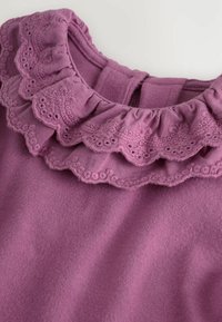 Lila Stoff mit doppellagigem, gerafftem Kragen, der mit detaillierten Blumenstickereien und gewellten Kanten verziert ist.