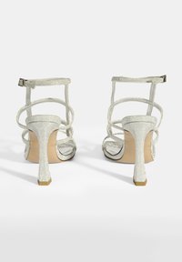 Silberner Glitzer-Peeptoe-Absatzschuhe mit dünnen Riemen und verstellbaren Knöchelriemen. Hoher Stiletto-Absatz mit beigem Fußbett und metallischen Details.