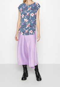 Blå topp med blommönster och korta ärmar, kombinerad med en fladdrig lavendel midi-kjol. Svarta knähöga stövlar fulländar outfiten.