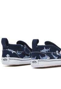 Zapatos de lona azul marino con un diseño de tiburón ballena; costuras y suela blancas; diseño sin cordones con una pestaña trasera y detalles del logo de Vans.