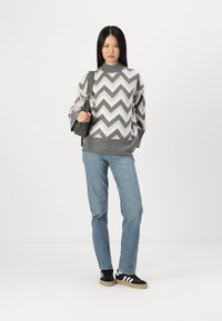 Grå og hvit genser med chevronmønster og høy krage, grå bunnstrikk, sammen med lyseblå jeans og svarte joggesko.