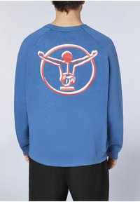 Blauer Pullover mit Raglanärmeln, auf der Rückseite mit einem großen rot-weißen Grafikdesign einer Figur in einem Kreis.