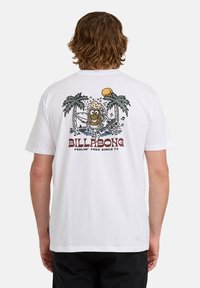 Person trägt ein weißes T-Shirt mit einem Comic-Bierglas, Palmen, Sonne und dem Text "Billabong Feelin' Free Since 73" auf dem Rücken.