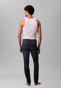 Balts tanktopi un tumši zilas pieguļošas džinsa bikses ar taisnu kāju piegriezumu, smalku šuvi un ādas ieliktni uz muguras vidukļa.