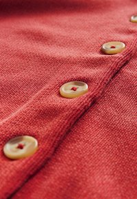 Red knit fabric featuring light brown buttons with red accents, displaying texture and visible stitching details.