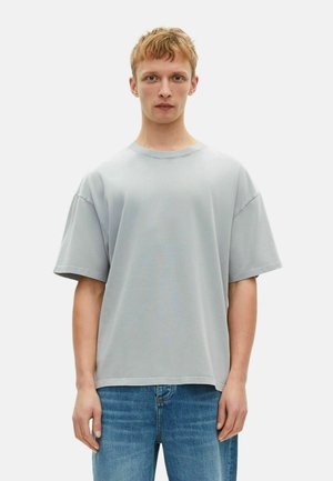 Lichtgrijs oversized t-shirt van katoen, met een ronde halslijn, verlaagde schouders en korte mouwen, gedragen met blauwe jeans.