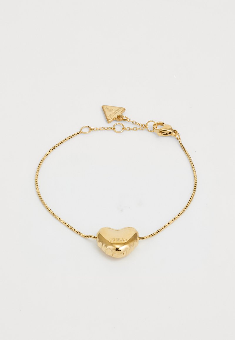Bracelet en or avec un charm en forme de cœur, présentant une surface texturée et le nom de la marque gravé. Chaîne en câble avec un fermoir en homard et une étiquette triangulaire.