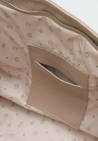 Beżowa torba z ekoskóry, wewnątrz z zamkiem błyskawicznym, posiadająca małą kieszonkę oraz wzorzystą satynową podszewkę w jasnym beżu z subtelnymi deseniami.