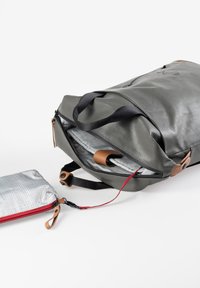 Donkergrijze leren tas met zwarte banden, voorzien van een geruite binnenvoering, bruine accenten en een klein zilvergrijs zakje met rode rits.