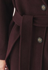 Bordový vlněný kabát se sakem pasem, viditelnými knoflíky, jemnou texturou a střihovým designem, se postranními kapsami a sklady.