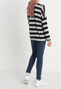 Schwarz-weiß gestreiftes Langarmoberteil mit lässiger Passform, kombiniert mit dunklen Jeans und weißen Sportschuhen.