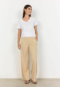 White V-neck T-shirt and beige wide-leg trousers, with a relaxed fit and side pockets. Footwear features a sleek design with black accents.