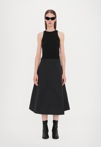 Musta ribattava tank top yhdistetty mustaan A-linjan hameeseen ja mustiin nilkkureihin. Mallilla on päällään mustat aurinkolasit. Yksinkertainen, minimalistinen muotoilu.