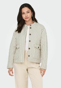 Gequilted jack in crème met verticale zwarte strepen, voorzien van een ronde hals, knoopsluiting en twee voorzakken. Gladde textuur.