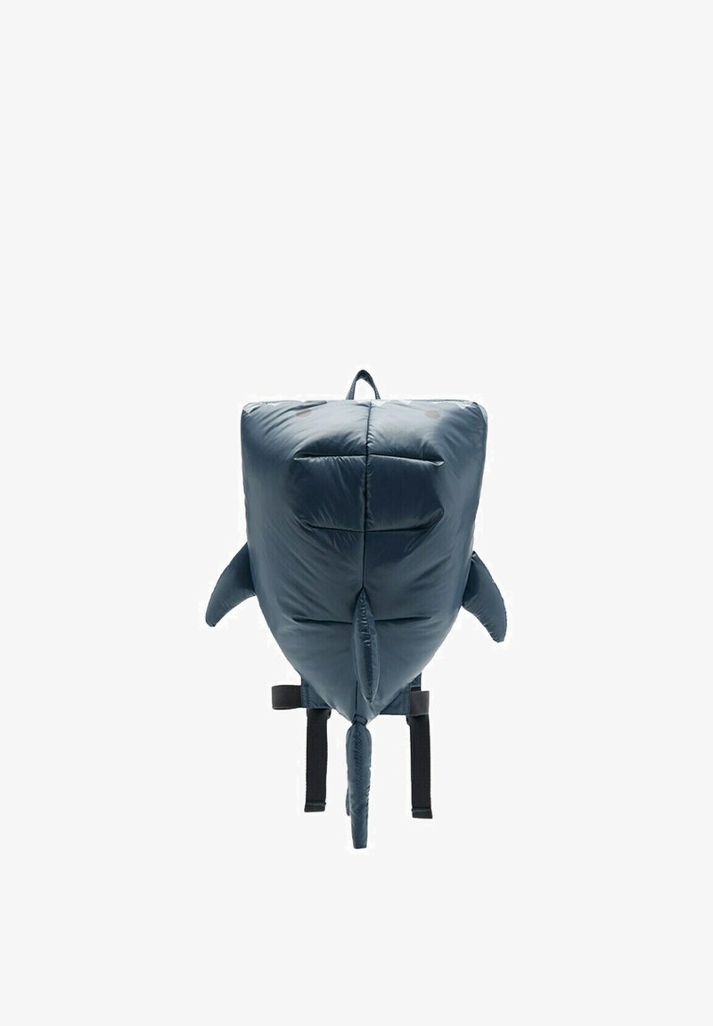 Sac à dos doux et rembourré en forme de requin bleu avec nageoires, queue et bretelles noires réglables sur fond blanc.