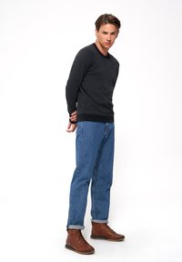 Granatowy sweter z teksturowanym wzorem, zestawiony z jasnoniebieskimi dżinsami i brązowymi butami sznurowanymi, z podwiniętym mankietem i prostym designem.