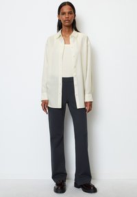 Off-white skjorte med avslappet passform, sammen med mørkegrå utsvingte bukser og kraftige svarte støvler. Glatt tekstur, minimalistisk design.