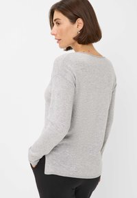 Grauer Strickpullover mit langen Ärmeln, rundem Ausschnitt, leicht strukturiertem Stoff und seitlichen Schlitzen, kombiniert mit schwarzen Hosen.