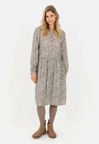Blomstret kjole i grå med knapfront, lange �ærmer og elastisk talje. Matchet med brune ankelstøvler og grå strømpebukser.
