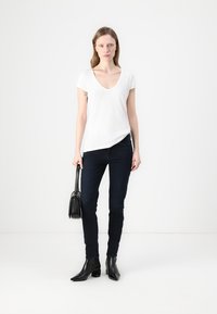 Camiseta blanca de cuello en V, jeans oscuros ajustados, botas negras hasta el tobillo y un pequeño bolso negro. Diseño minimalista con textura de tela suave.