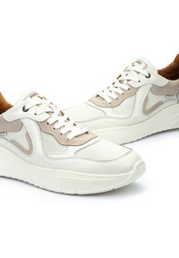 Zapatillas blancas y beige con paneles de malla y ante, puntera redonda, cuello acolchado, cordones planos y suela de goma texturizada. Logo de la marca en el lateral.
